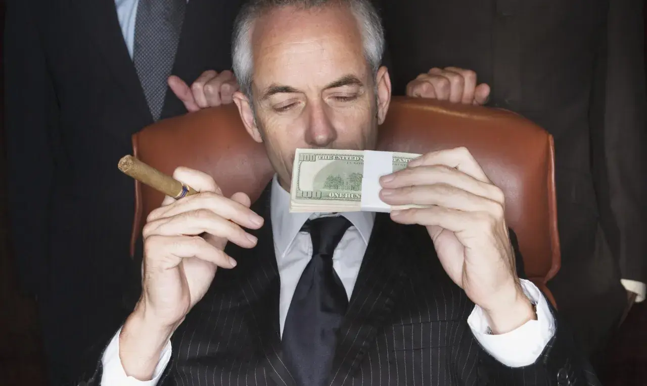 Mężczyzna w garniturze z cygarem w dłoni wącha stos banknotów. Sekret jak że 100 tys zrobić milion?