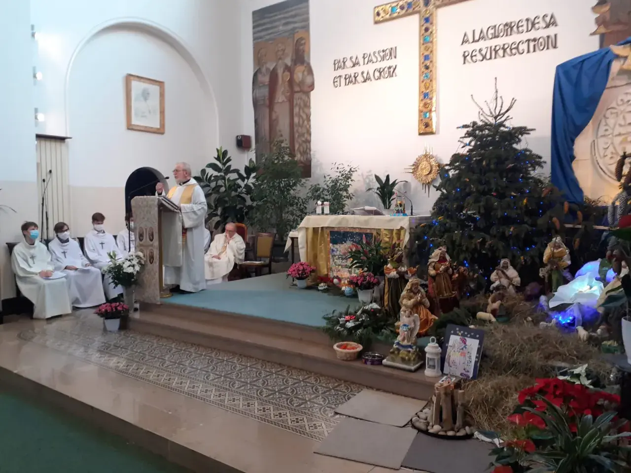 Uroczystość w kościele z kapłanem przy pulpicie i szopką bożonarodzeniową. Święta Genowefa w centrum uwagi.