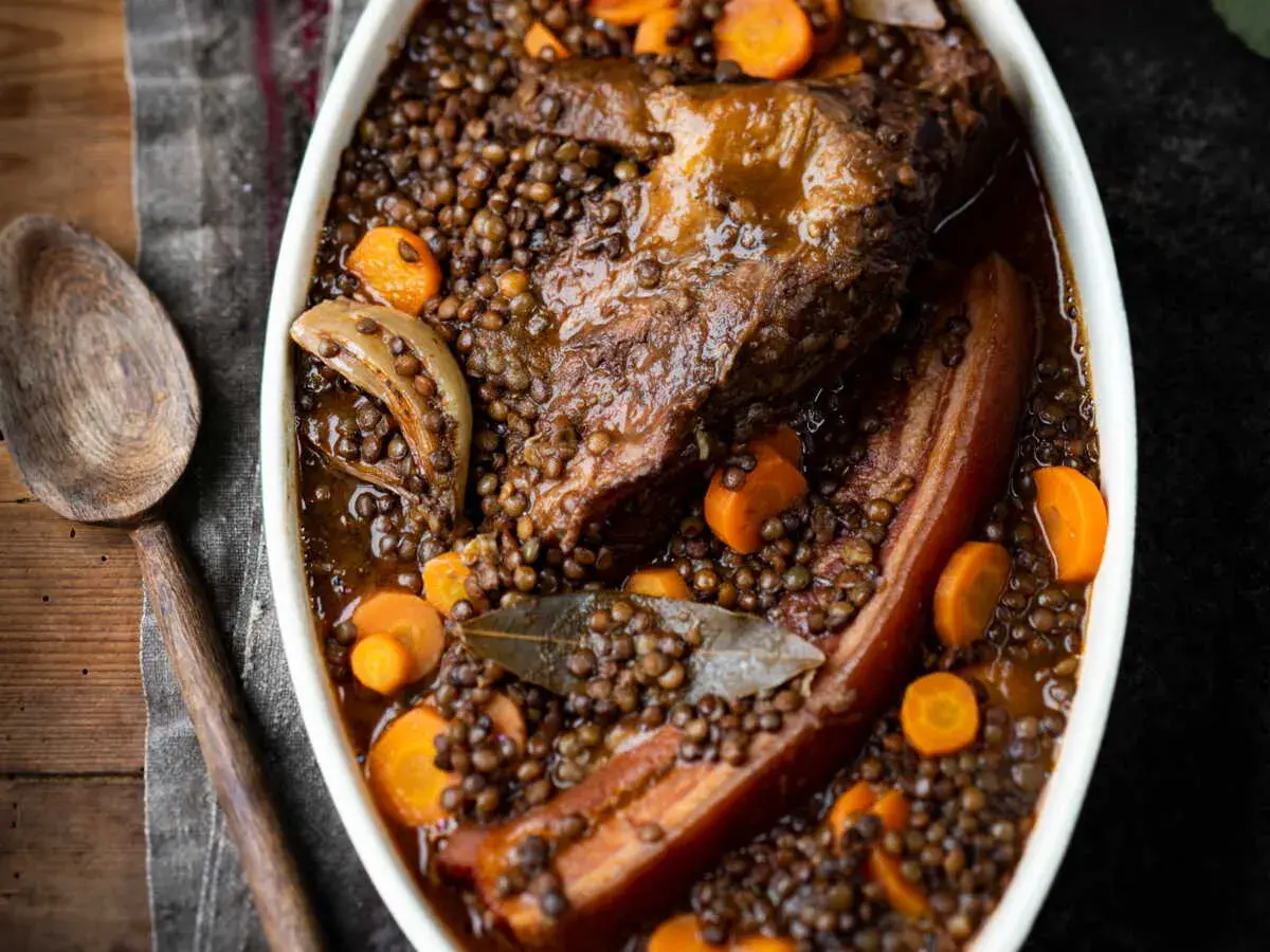 Un plat réconfortant de petit salé aux lentilles, avec des morceaux de viande savoureux, des carottes et des oignons, prêt à être servi.