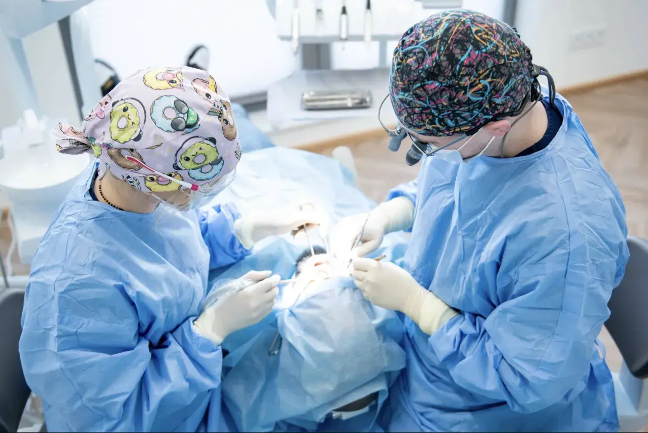 Chirurdzy stomatologiczni wykonują zabieg augmentacji kości, precyzyjnie pracując w jamie ustnej pacjenta.