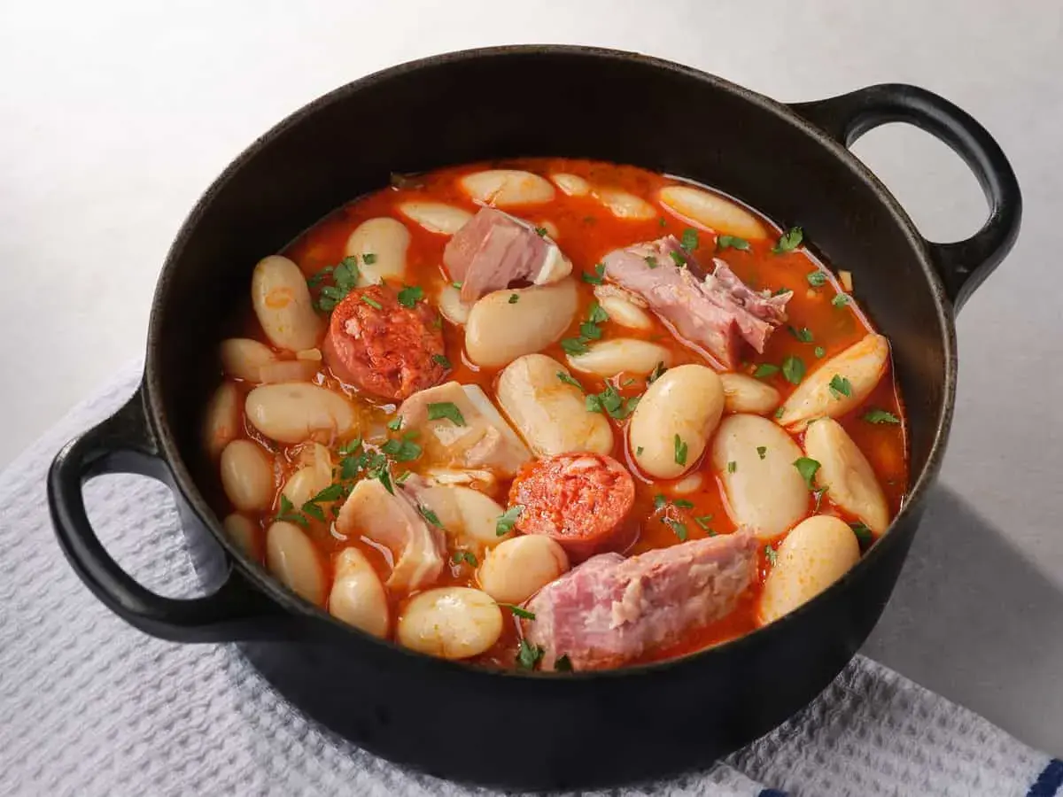 Judiones de la granja en cazuela negra, con chorizo, tocino y perejil picado. Un plato reconfortante y lleno de sabor.