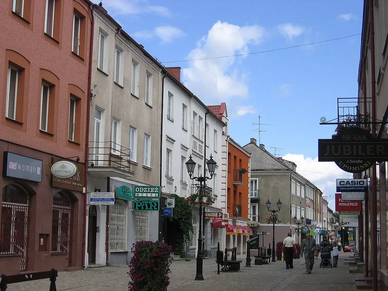 Ulica w Polsce, z kamienicami po obu stronach. Widać szyldy sklepów, m.in. "Jubiler" i "Casio". Kierunkowy 86 w Polsce.