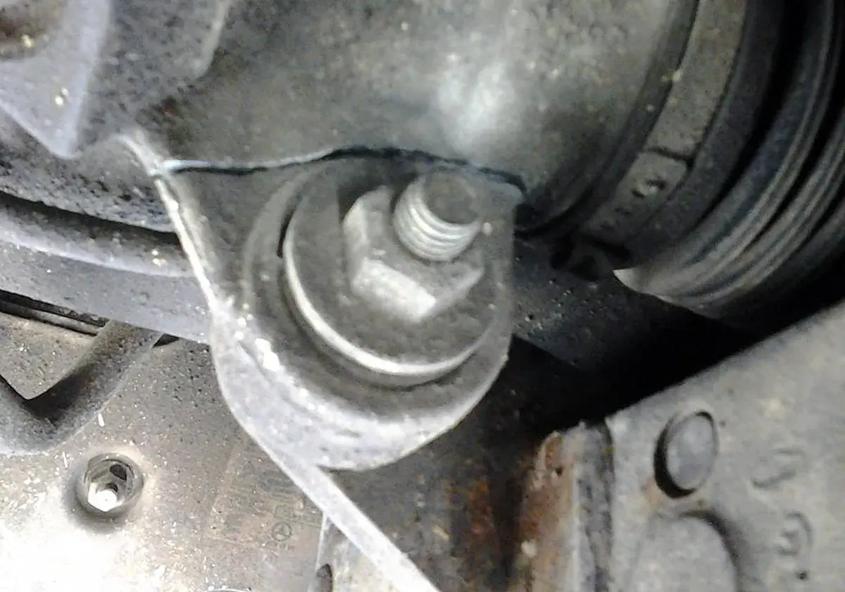 Soporte metálico con un perno hexagonal sujetando una pieza del motor, cerca de un componente que podría ser parte del volante de dirección.