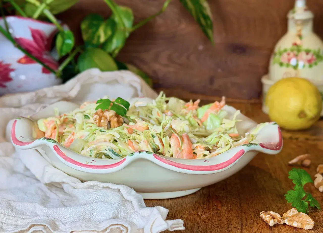 Deliciosa ensalada de col cremosa con zanahoria rallada, coronada con nueces y perejil. Perfecta para acompañar cualquier comida.
