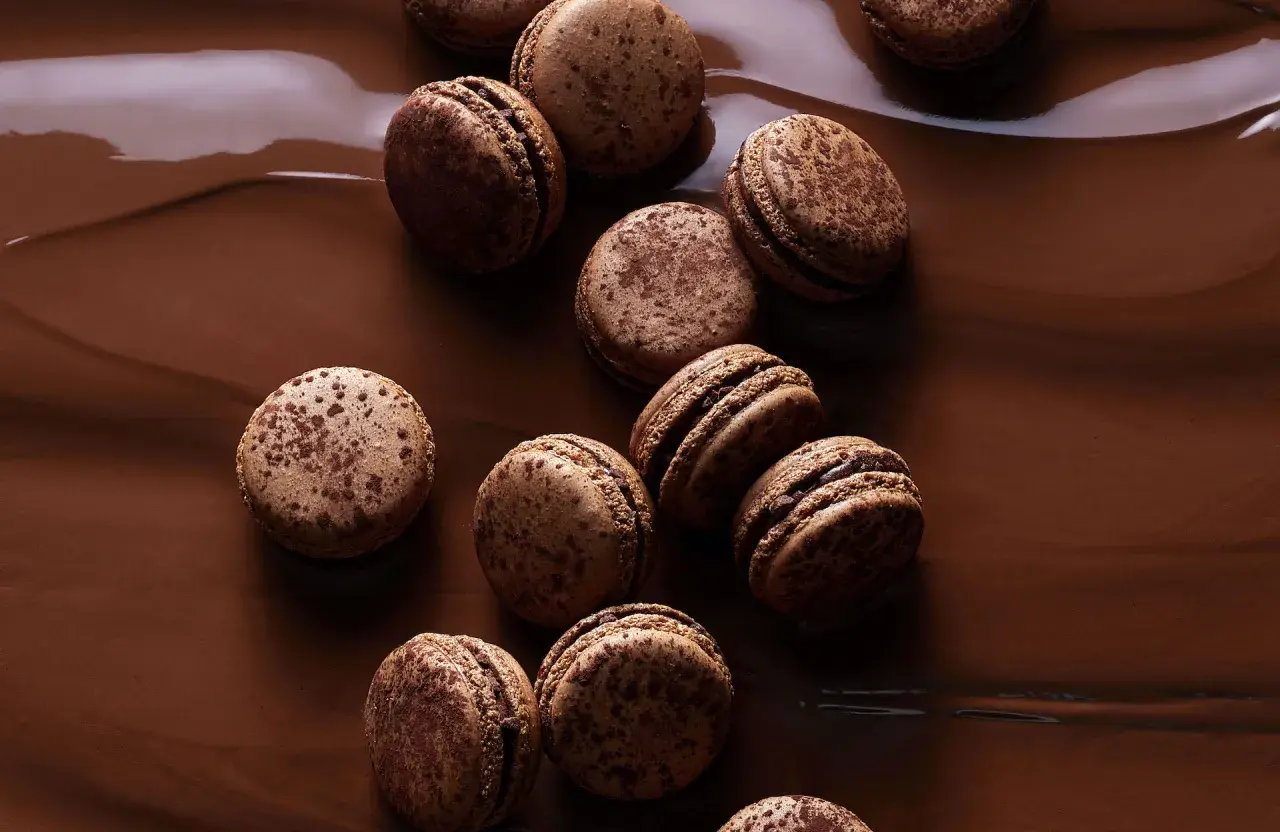 Douceurs chocolatées pour une recette macaron chocolat parfaite. Ces macarons aux éclats de cacao reposent sur un lit de chocolat fondant.