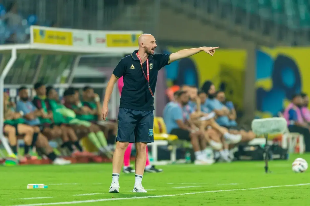 Tomasz Tchórz, trener, wskazuje kierunek na boisku. Za nim siedzą zawodnicy na ławce rezerwowych.