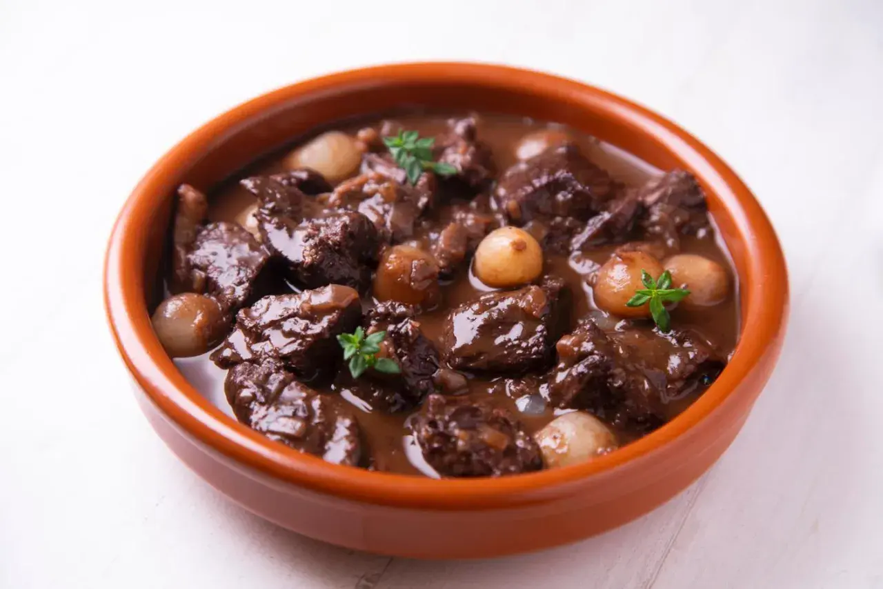 Herzhaftes Spezzatino di manzo mit kleinen Zwiebeln und Kräutern in einer Terrakotta-Schale.