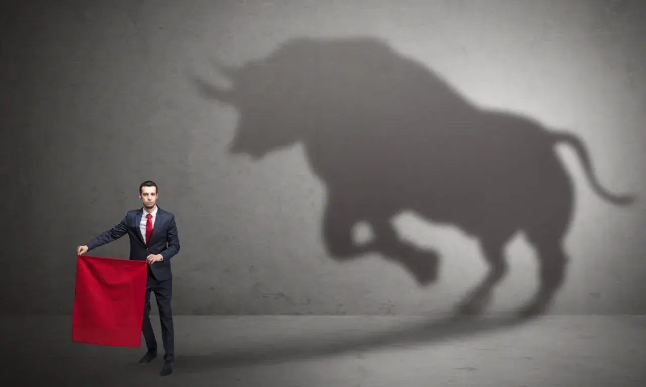Un hombre con traje y corbata roja sostiene una tela roja, mientras la sombra de un toro irrumpe en la pared. ¿Qué significa soñar con toros?