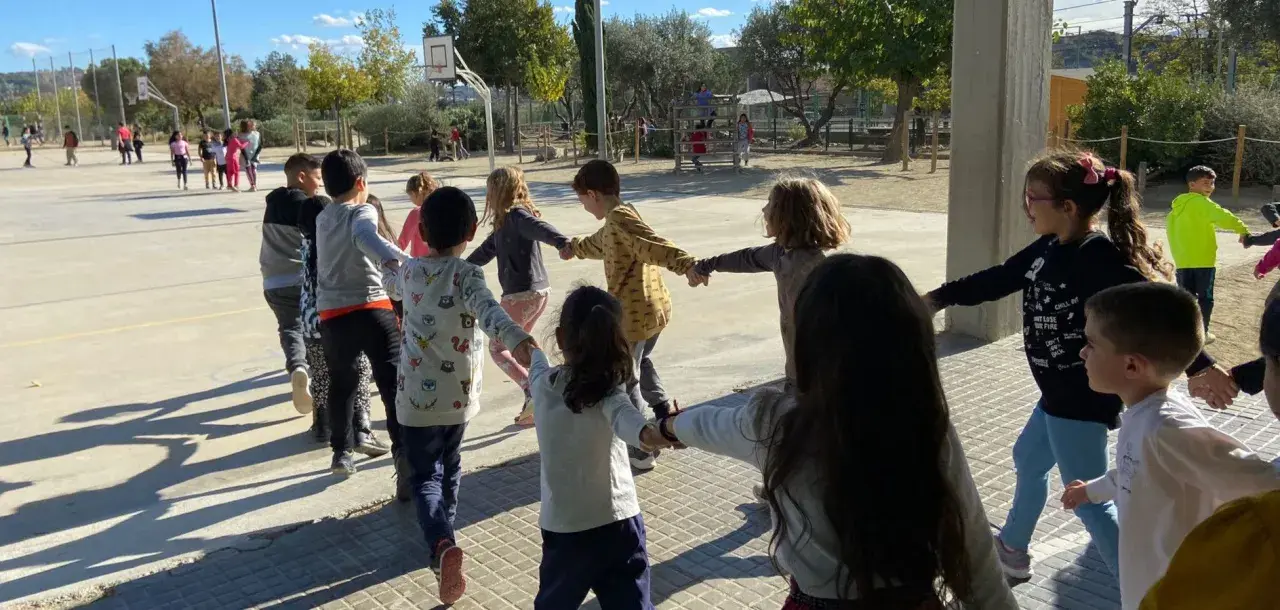 Niños jugando en círculo, tomados de la mano, en una actividad de juegos de conocimiento del medio al aire libre.