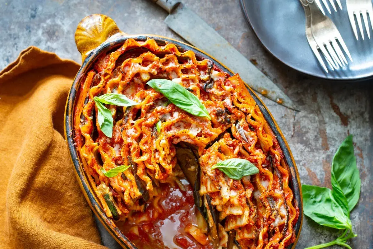 Lasagne aubergine gratinée, garnie de basilic frais, dans un plat ovale. Un délice italien réconfortant.