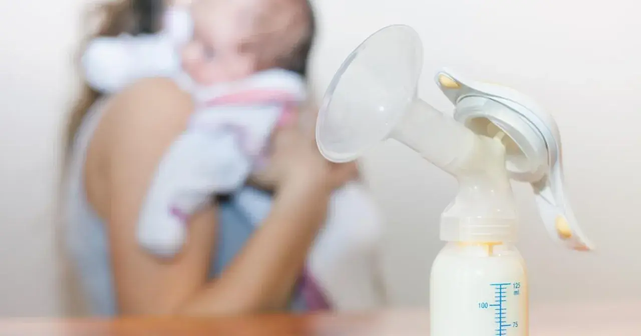 Laktator z butelką mleka, w tle mama z dzieckiem. Nawał pokarmu w której dobie to wyzwanie, ale dzięki niemu maluch ma co jeść.