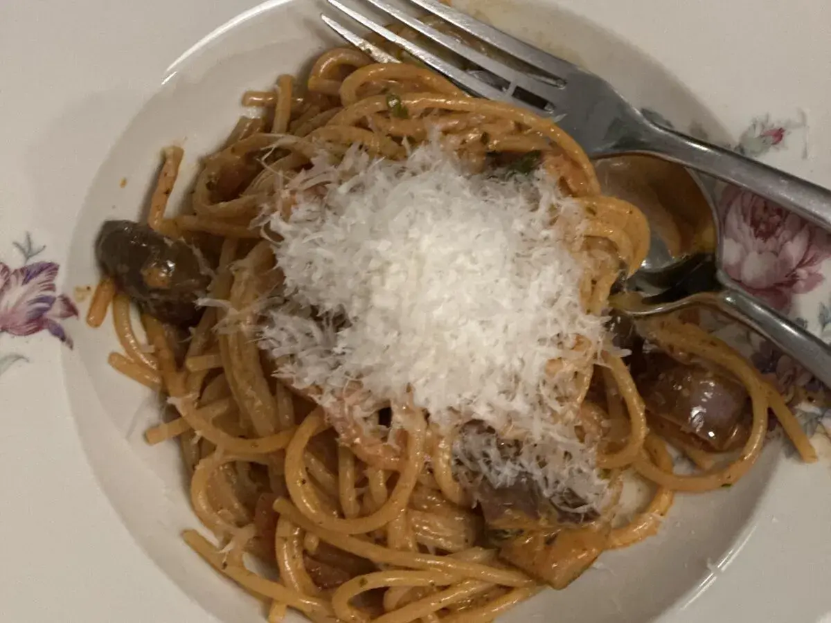 En tallrik med pasta alla norma, toppad med riven ost. Auberginebitar syns bland spaghettin.