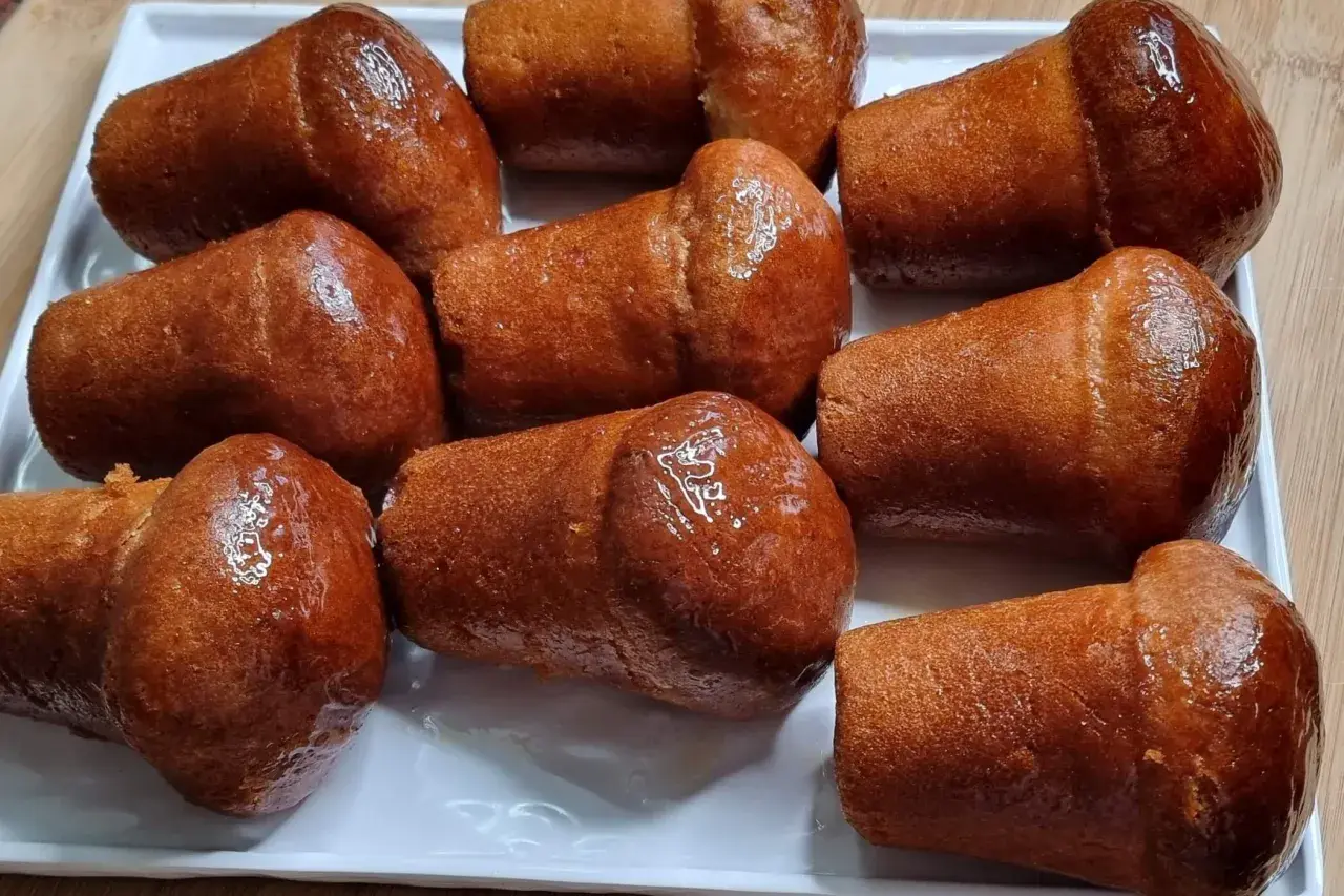 Un vassoio bianco pieno di deliziosi babà dorati, inzuppati in uno sciroppo lucido.