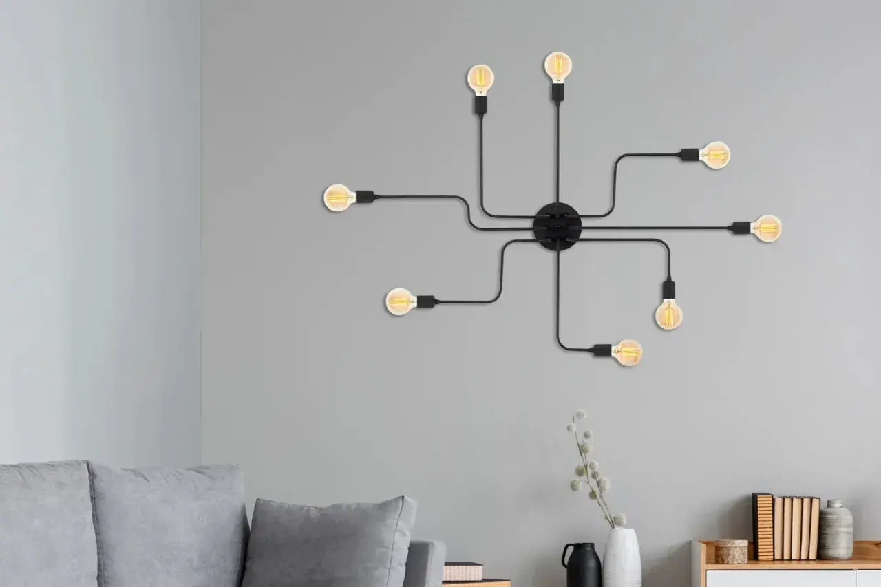 Un aplique de pared negro con siete bombillas Edison, que parece una araña moderna, ilumina la pared gris sobre un sofá.