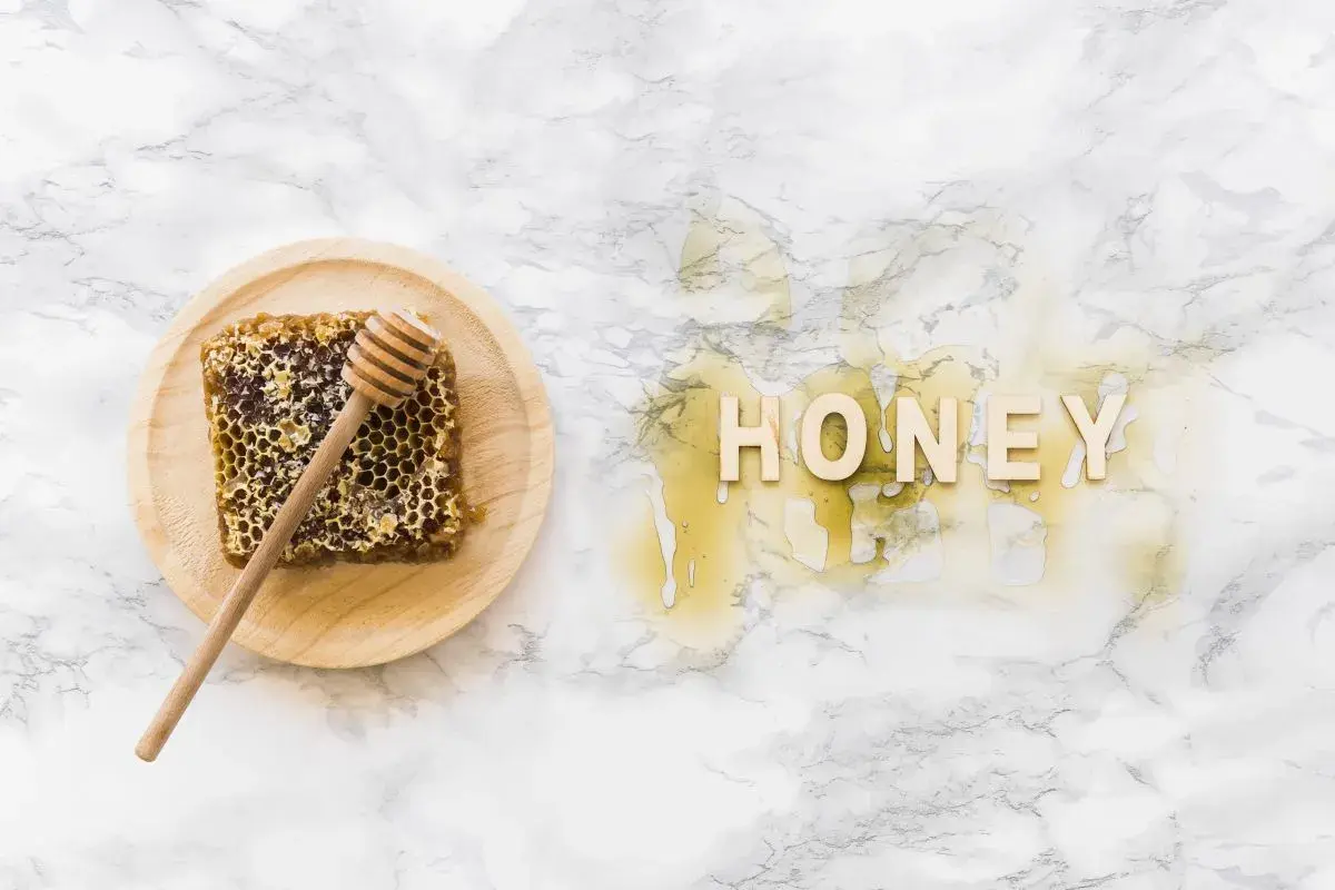 Plaster miodu z drewnianym mieszadełkiem na talerzyku i napis "HONEY" z miodu na marmurowym tle.