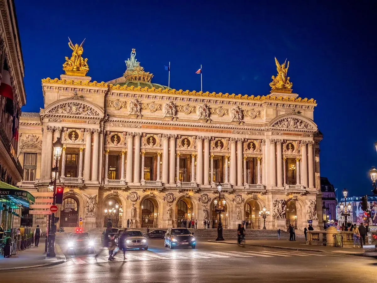 Słynny teatr w Paryżu, Opera Garnier, lśni w nocnym świetle. Złote rzeźby i bogata fasada zapraszają na wieczór pełen wrażeń.