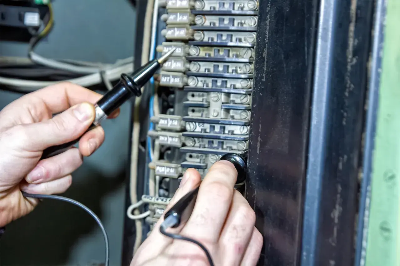 Ręce sprawdzają bezpieczniki w skrzynce elektrycznej. Czy bezpiecznik może się zepsuć? Tak, dlatego warto je kontrolować.