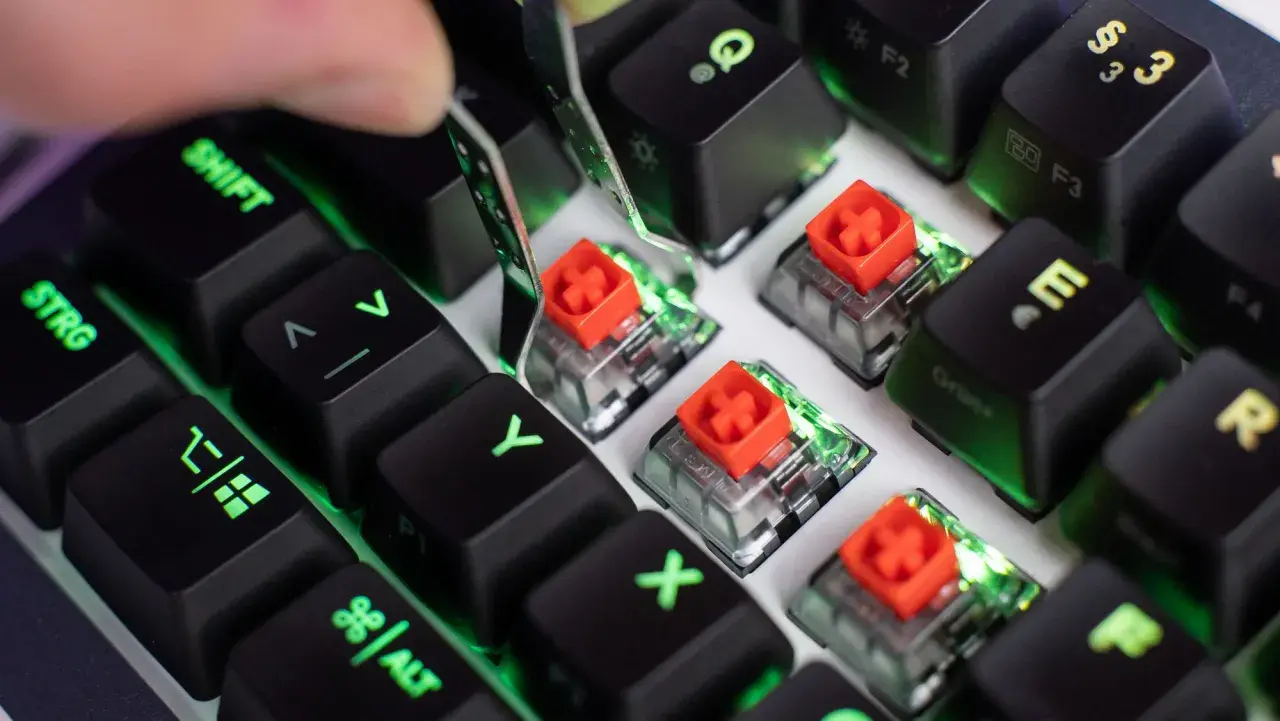 Nahaufnahme von Tastatur-Switches mit roten Kappen, die Unterschiede zeigen. Grüne Beleuchtung schimmert durch.