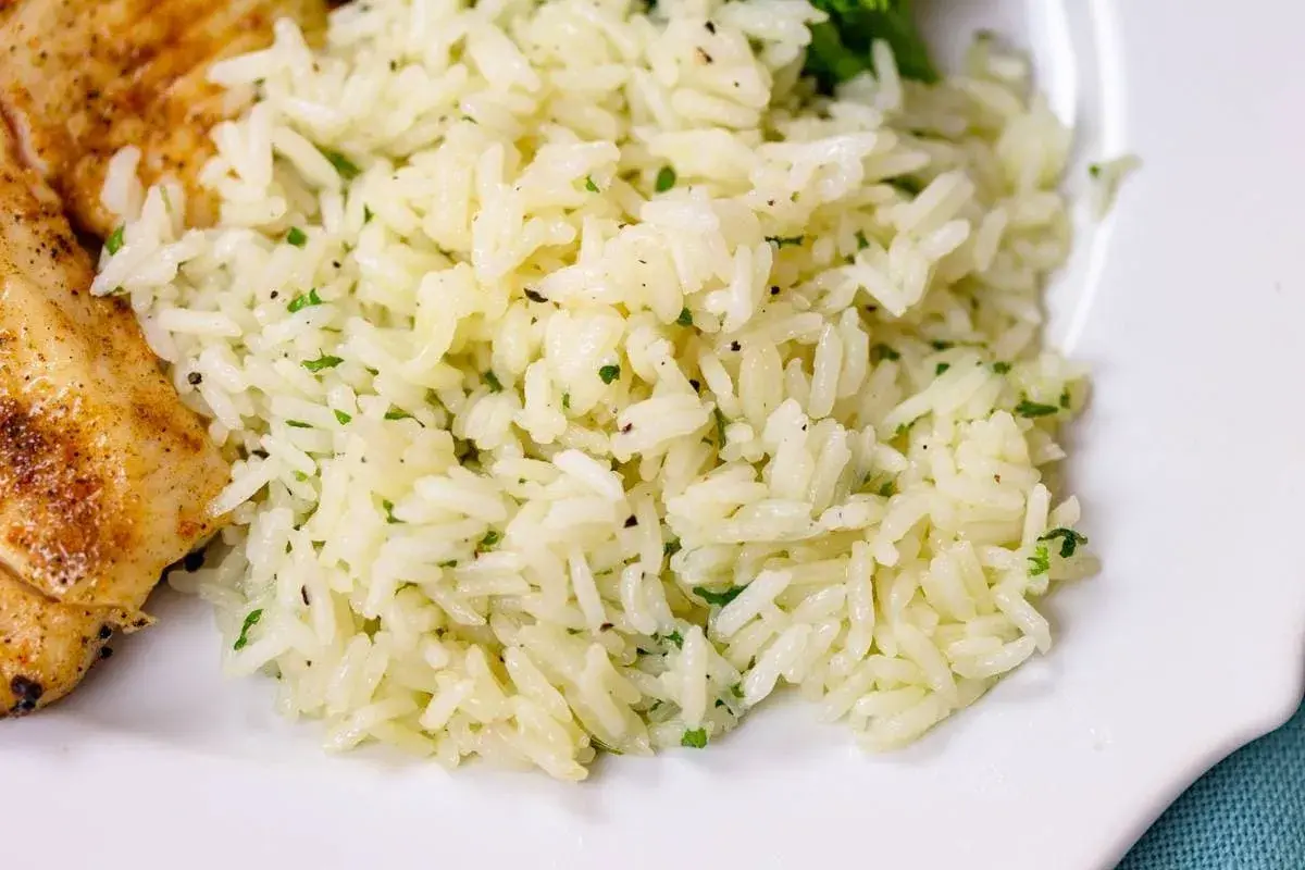Fluffy white rice with flecks of green herbs, perfect for a simple rice seasoning recipe. A side of grilled chicken is visible.