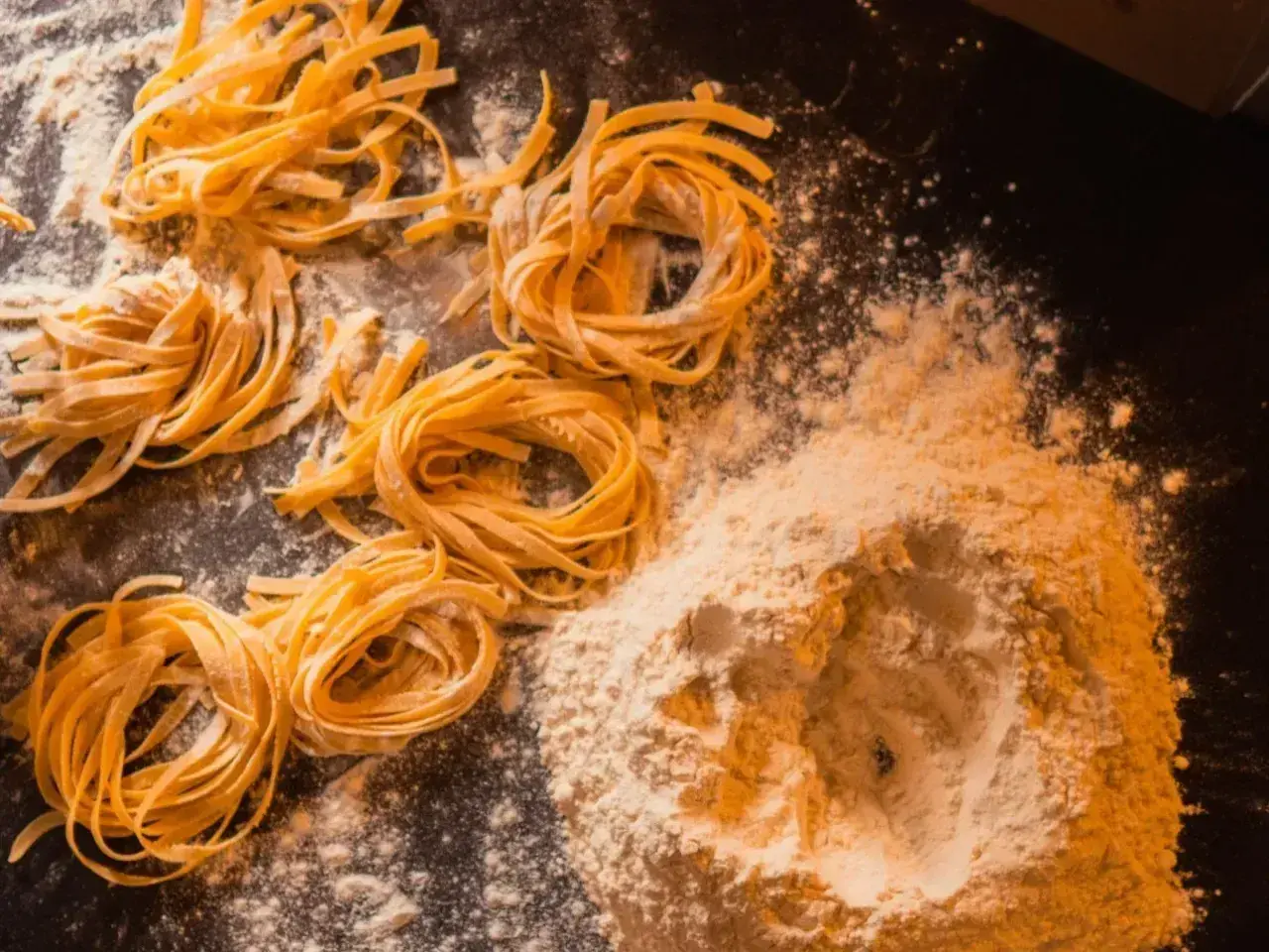 Domowy makaron, jak u babci! Świeże tagliatelle uformowane w gniazda, obok kopczyka mąki. Przepis babci na pyszne danie.