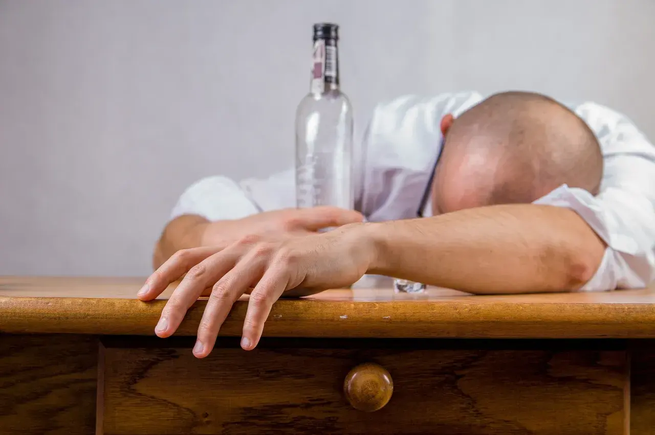 Mężczyzna śpi na biurku obok pustej butelki. Czy alkohol wypłukuje żelazo? To pytanie zadaje sobie wielu.