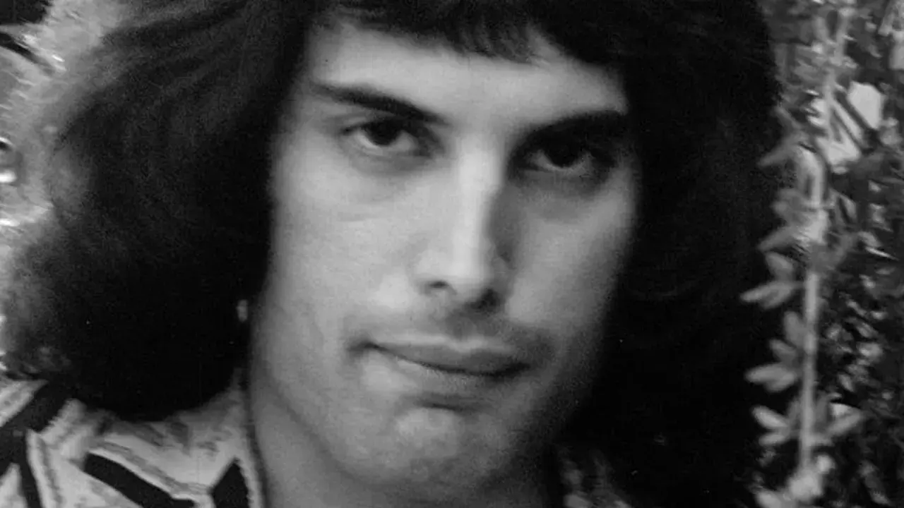 Zbliżenie na twarz młodego Freddiego Mercury'ego, którego prawdziwe imię to Farrokh Bulsara. Jego charakterystyczna fryzura i spojrzenie.