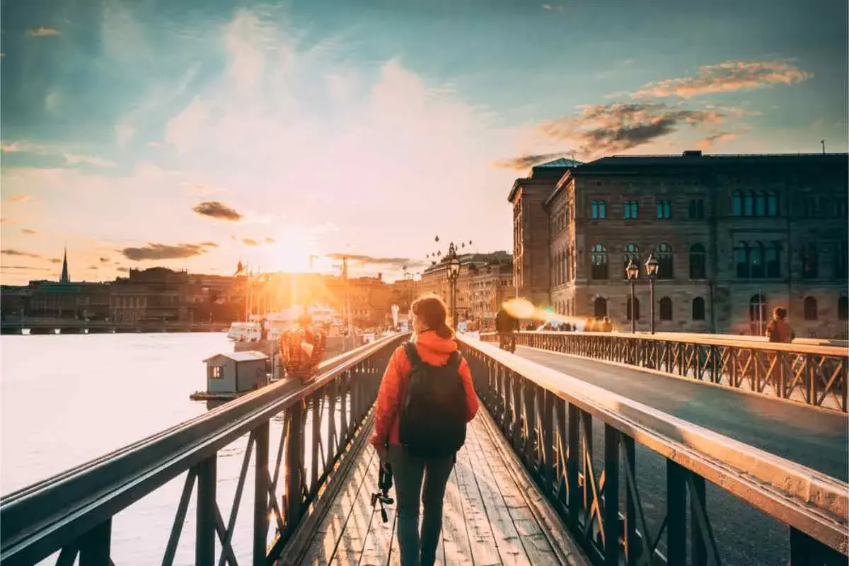 En person med ryggsäck promenerar i Stockholm vid solnedgången över vattnet.