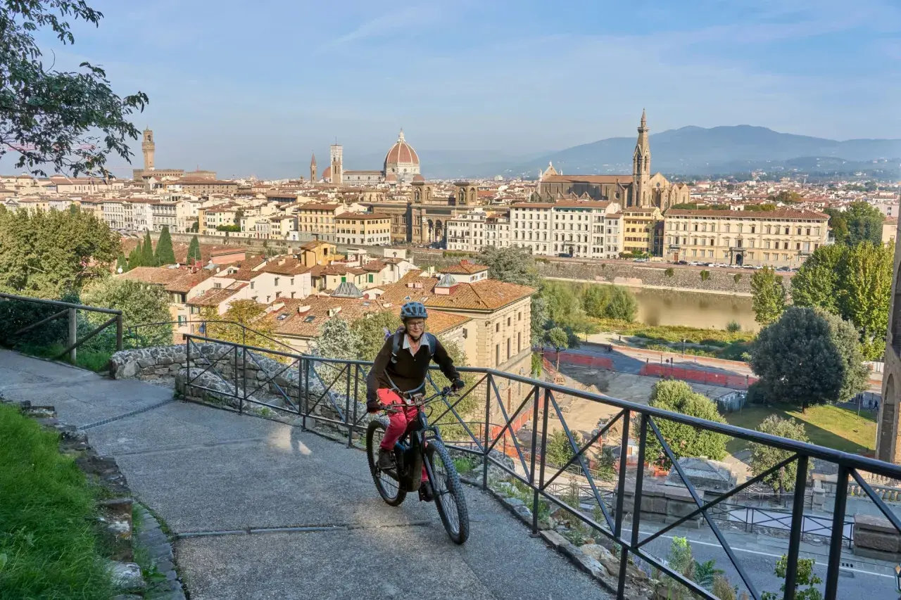 A woman enjoys an Italy bike tour, cycling with Florence's iconic skyline behind her.