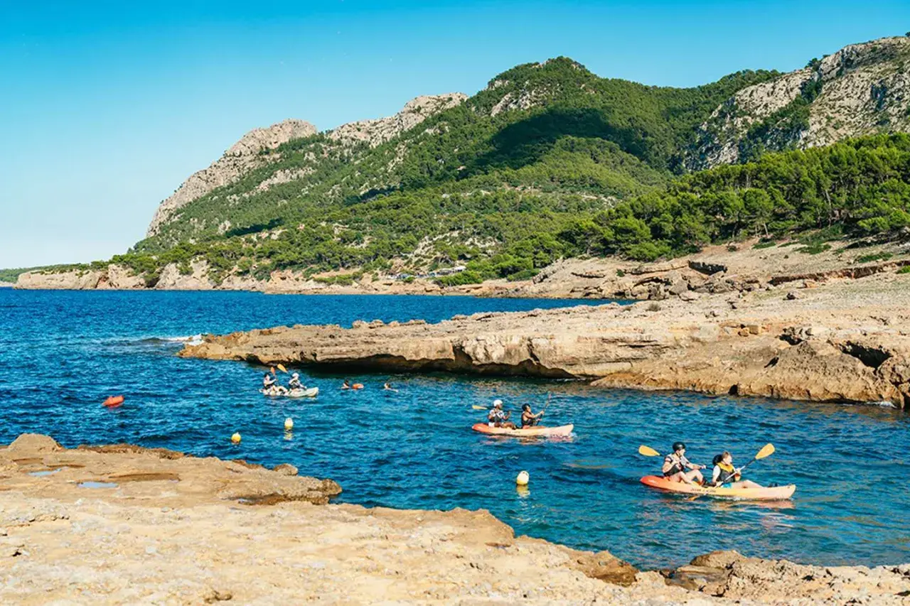 Kajakfahrer erkunden eine felsige Bucht mit türkisfarbenem Wasser und bewaldeten Bergen im Hintergrund. Perfekt für die Frage: wohin auf Mallorca?