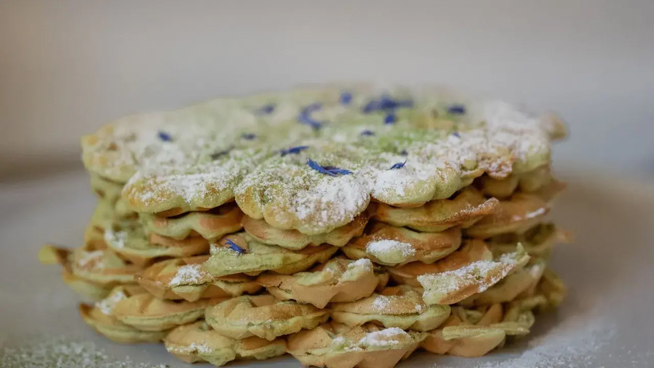 Ein Stapel leckerer Matcha Waffeln, bestäubt mit Puderzucker und verziert mit blauen Blütenblättern.