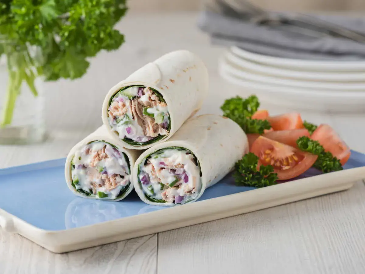 Trois wraps au thon crémeux, garnis de thon, oignons rouges et concombre, servis avec des quartiers de tomates et du persil.