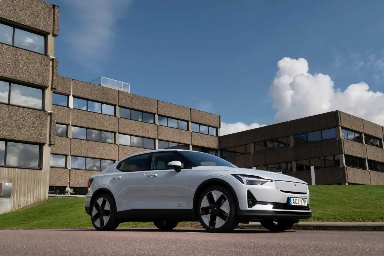 Vit Polestar 2 parkerad framför ett modernistiskt betonghus. Bilen är redo för en polestar 2 testkörning i solsken.
