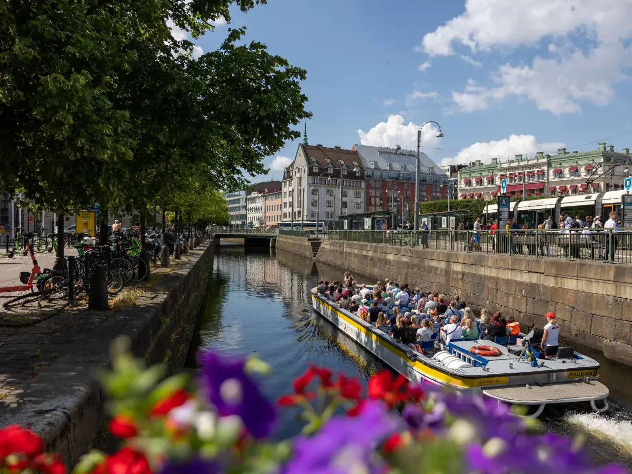 En paddanbåt med turister glider fram på kanalen i Göteborg. Blommor i förgrunden ger en färgklick.