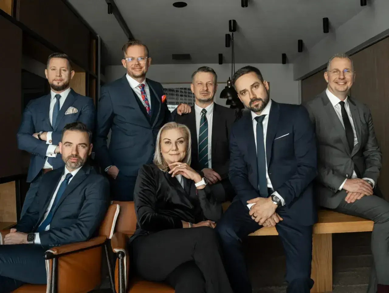 Grupa siedmiu profesjonalistów w garniturach, w tym jedna kobieta, pozuje do zdjęcia.