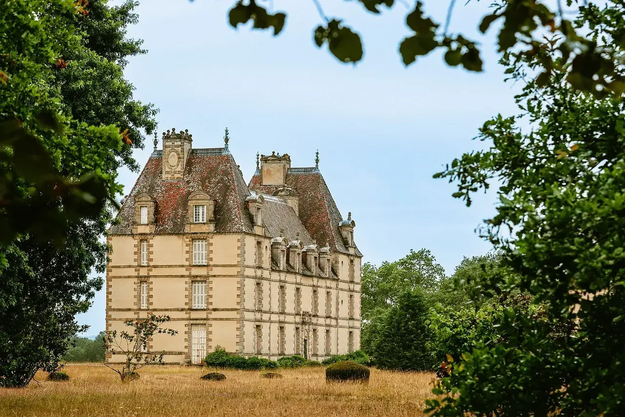 Un majestueux chateau abandonné se dresse au milieu d'une prairie dorée, entouré d'arbres verdoyants.