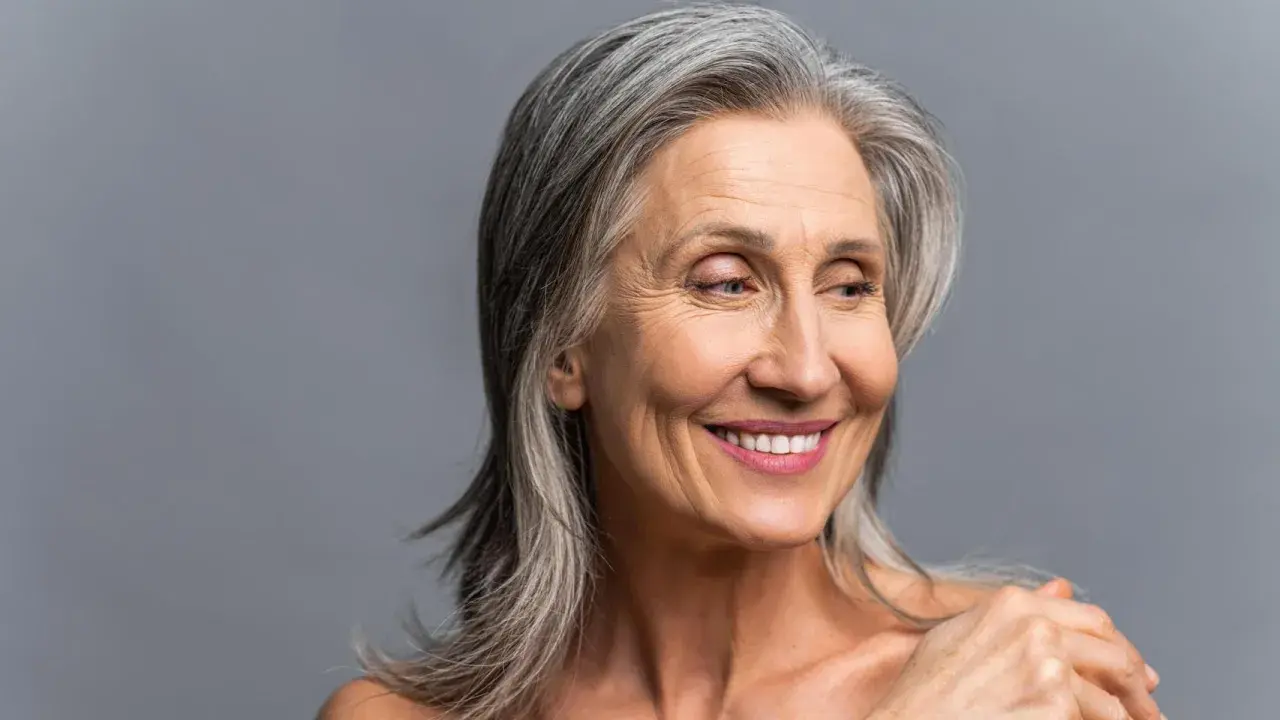 Mujer sonriente con cabello plateado, sus canas brillan con sabiduría y experiencia.
