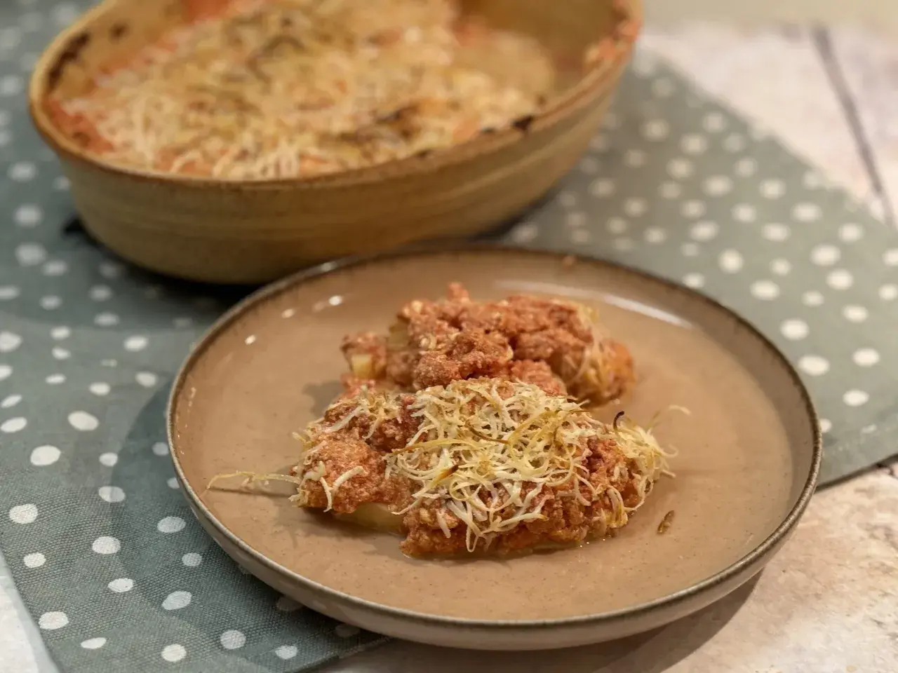 Dos porciones de gnocchi alla romana gratinados con queso, servidos en un plato marrón sobre un mantel de lunares.