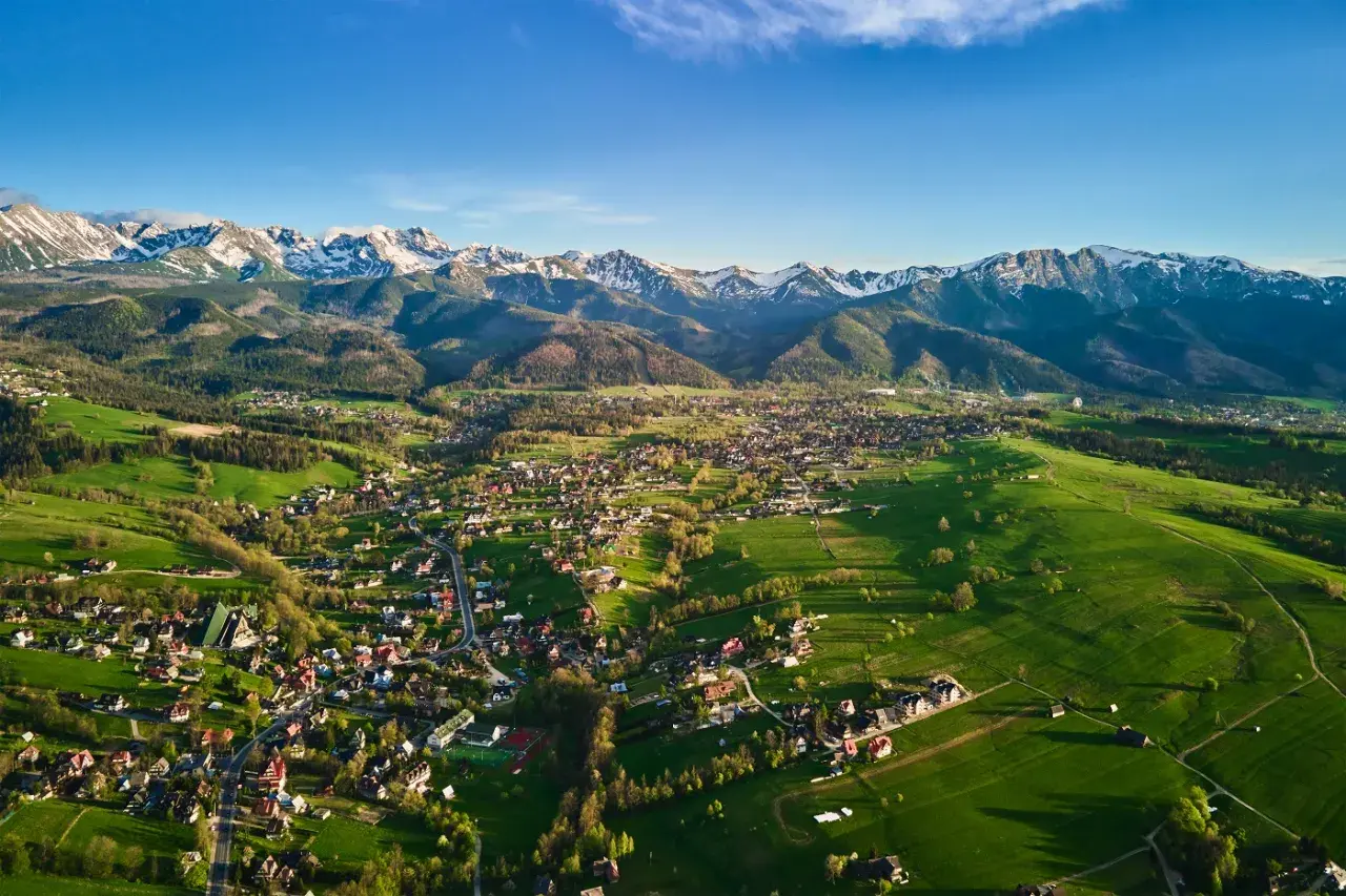 Widok na Zakopane i Tatry. Zielone łąki, zabudowania i ośnieżone szczyty tworzą malownicze okolice Zakopanego atrakcje.