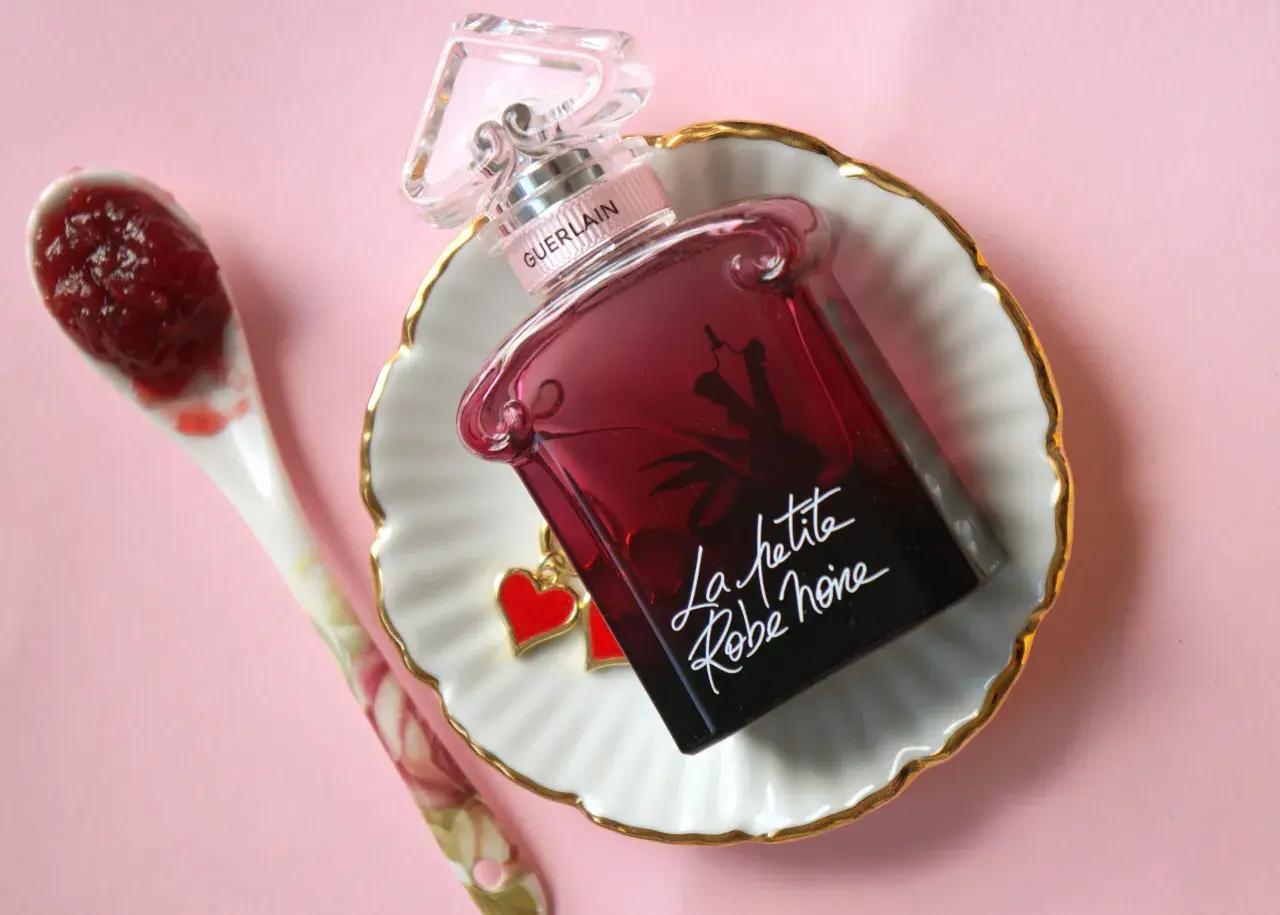 Elegancka buteleczka perfum Guerlain La petite robe noire z uroczymi serduszkami, obok łyżeczka z dżemem.