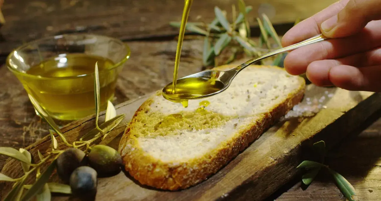 Olio d'oliva versato su pane, con olive e rametti d'ulivo. Un assaggio dei sapori autentici degli oleifici puglia.