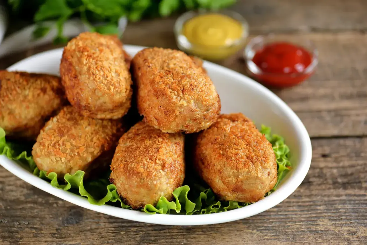 Six croquettes de crevette dorées et croustillantes sur un lit de laitue, avec des sauces moutarde et ketchup en arrière-plan.