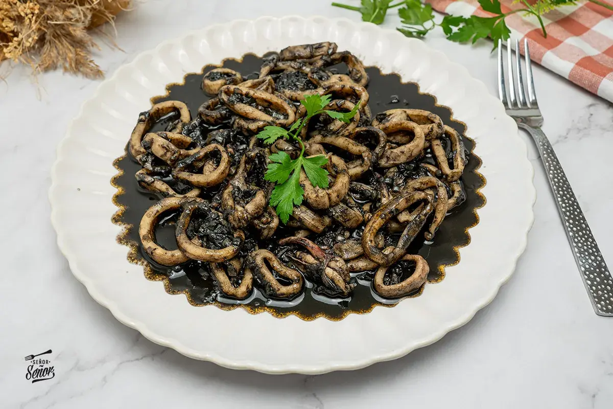 Plato de calamares en su tinta, con anillas tiernas y sabrosas, decorado con perejil fresco. Un clásico irresistible.
