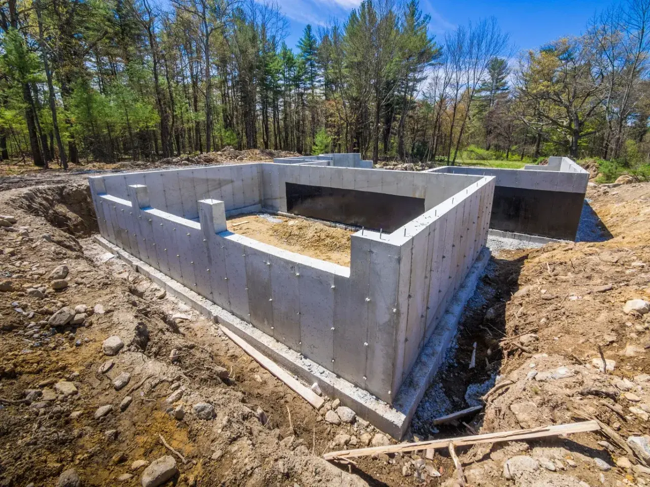 Solidny ruszt fundamentowy z betonu, gotowy na budowę domu. Otoczony ziemią i drzewami, czeka na kolejne etapy prac.