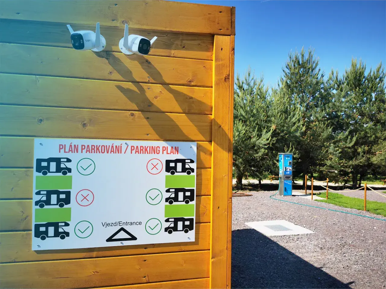Tablica z planem parkowania dla kamperów, z zaznaczonymi miejscami dozwolonymi i zakazanymi. Dwie kamery monitoringu nadzorują teren.