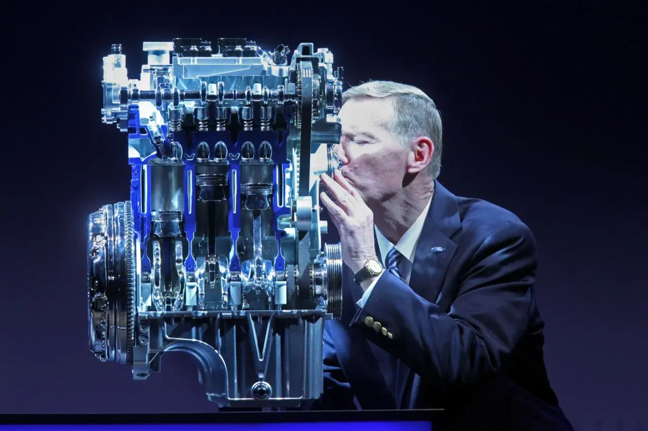 Mężczyzna w garniturze całuje silnik Forda. Wiele osób szuka **1.0 ecoboost opinie** przed zakupem.
