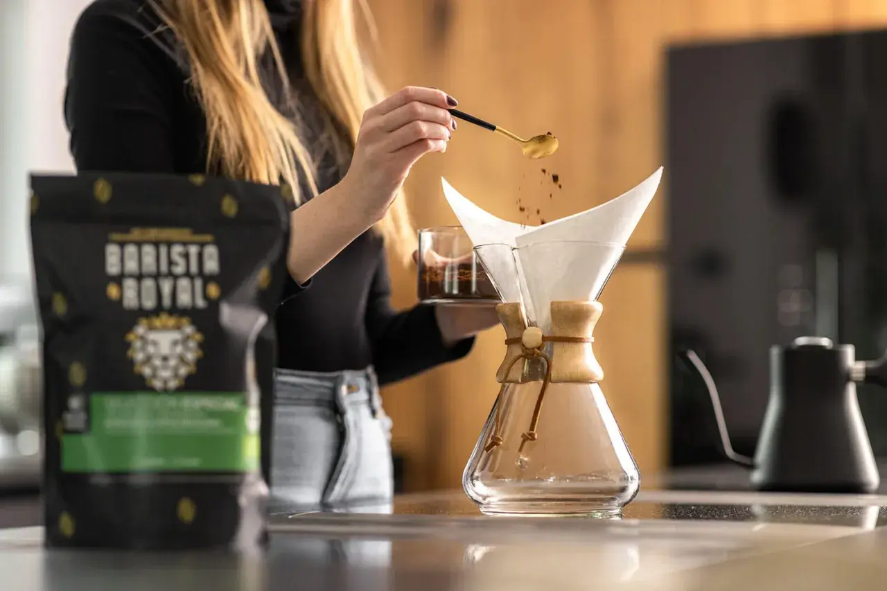 Eine Frau gibt mit einem Löffel Kaffeepulver in einen Chemex-Filter. Die richtige **Filterkaffee Menge** ist entscheidend für den perfekten Geschmack.