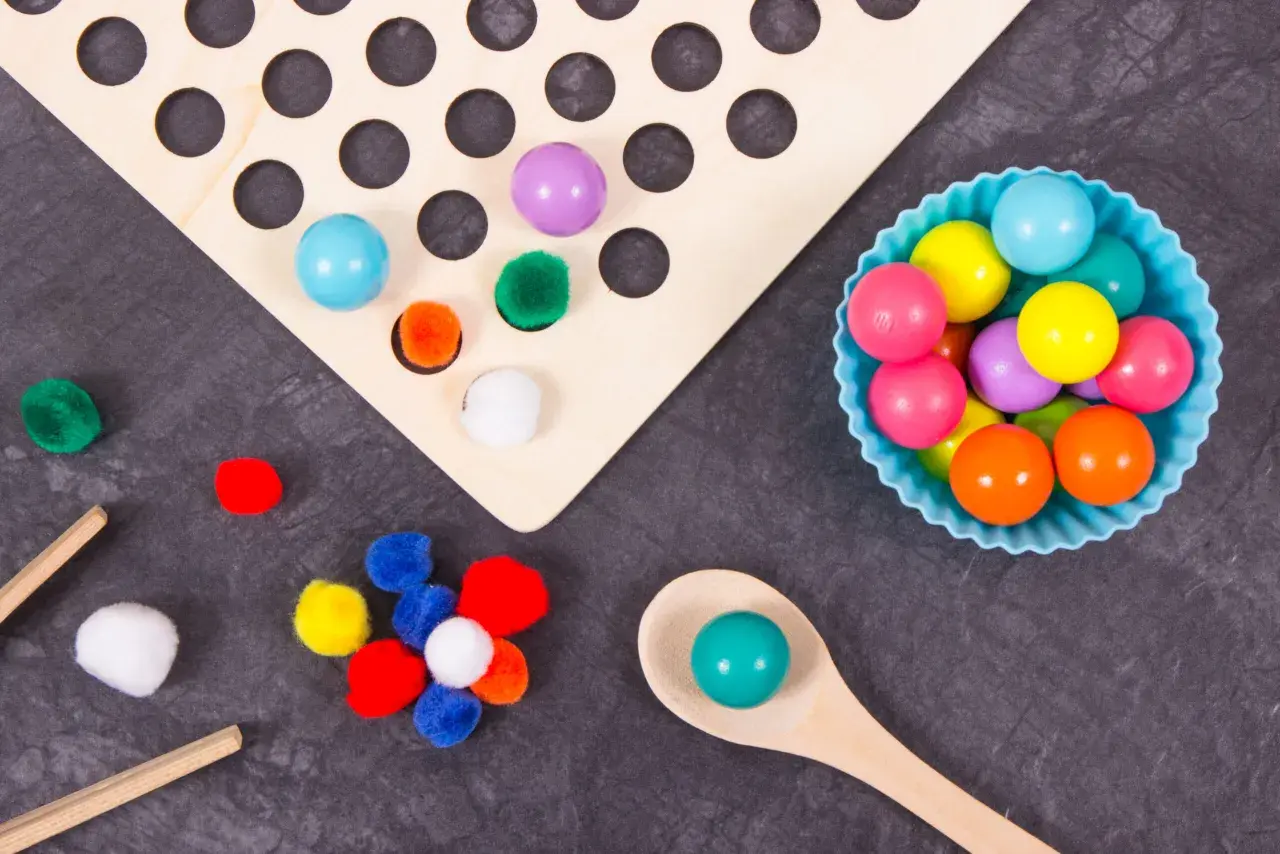 Juego heuristico materiales: pompones, bolas de colores y cuchara de madera para explorar texturas y formas.
