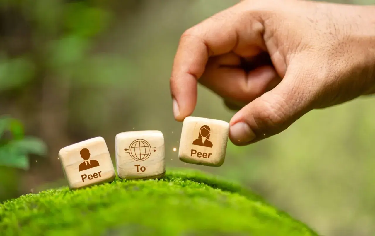 Dłoń układa kostki symbolizujące p2p: "Peer To Peer".