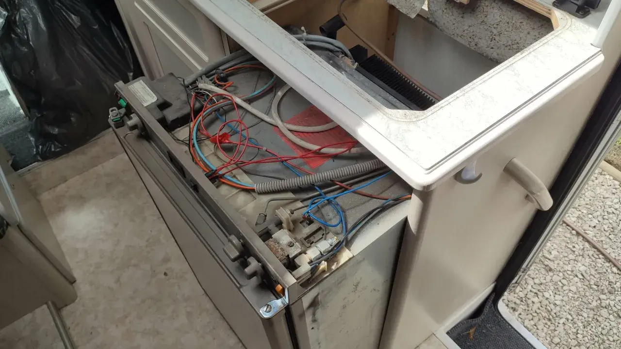 Réparation du frigo camping-car 12v 220v gaz Dometic en panne. Câblage apparent et composants exposés.