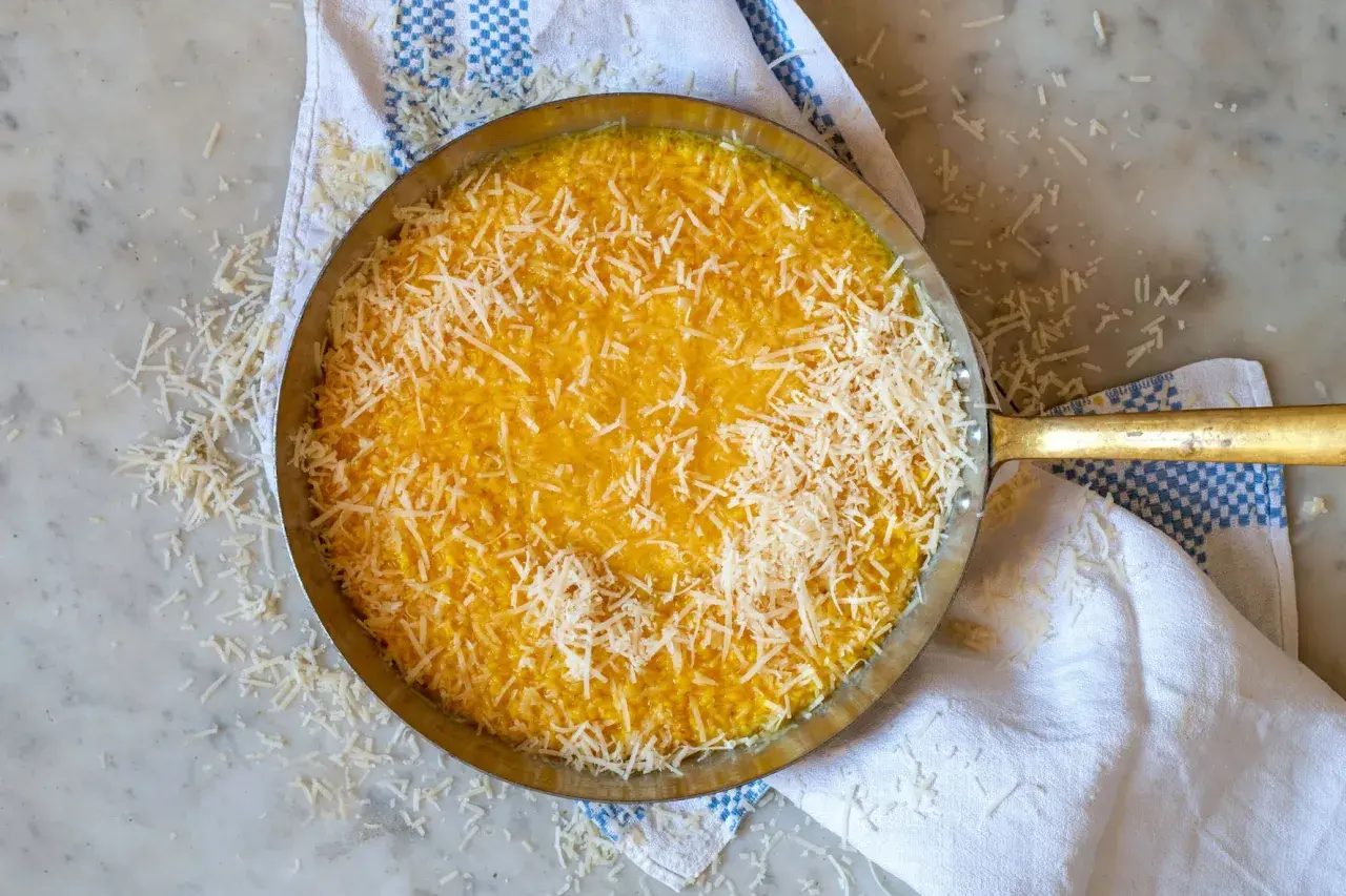 En gyllene risotto milanese, toppad med riven parmesan, i en metallpanna på en marmorskiva.